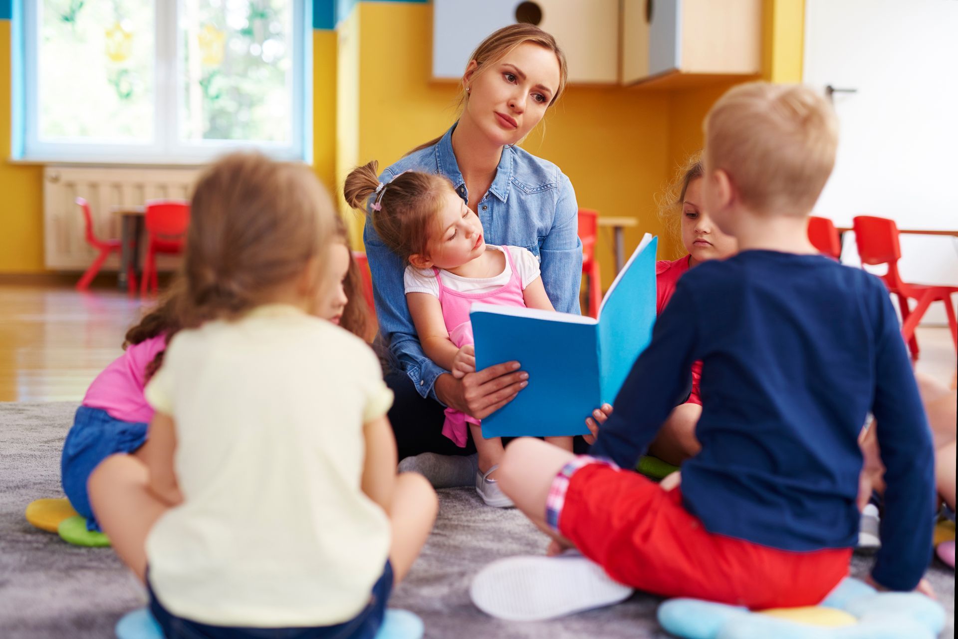 Teacher reading a blue book to children sitting on a classroom rug