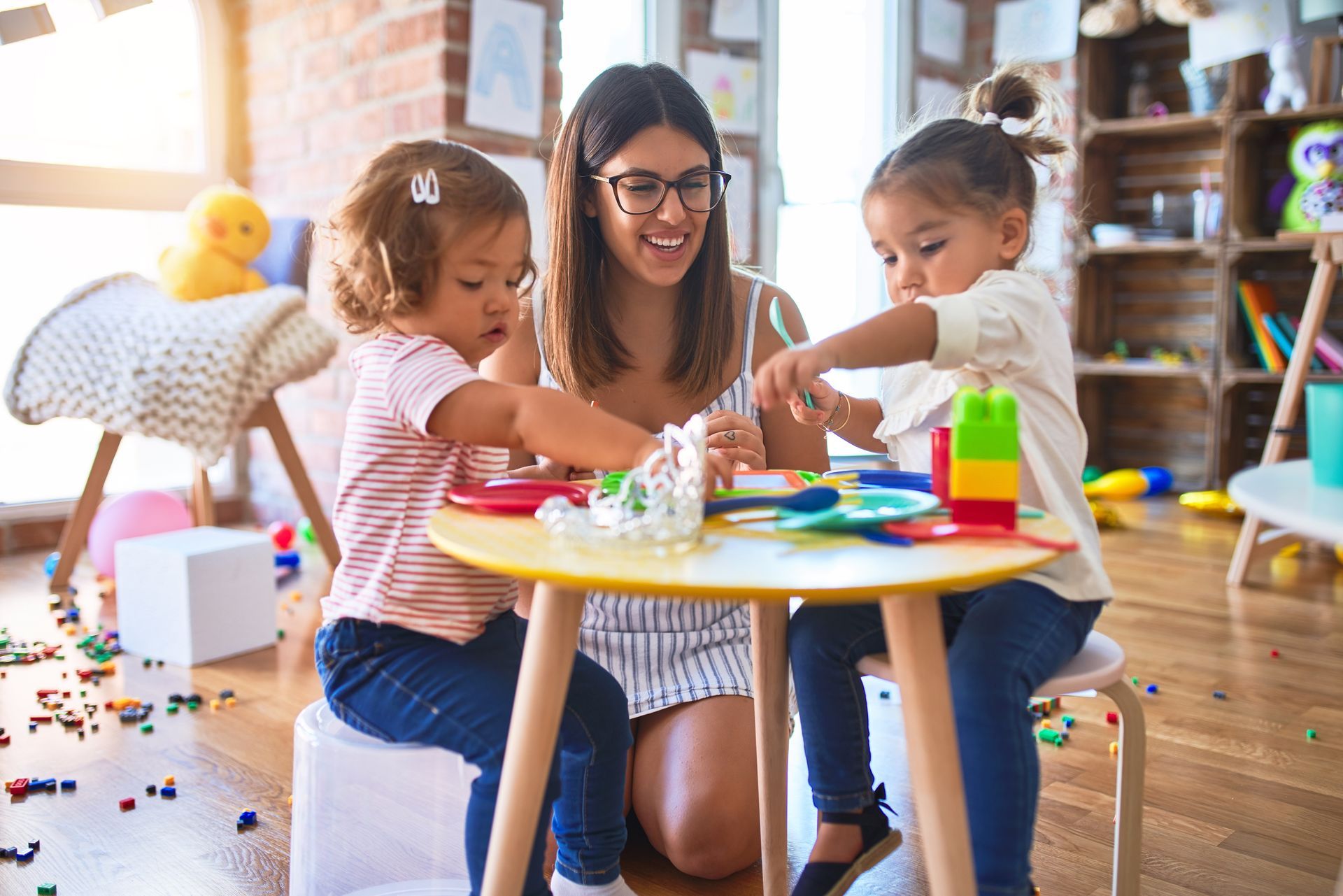 Adult and two children doing crafts at a small table in a bright playroom