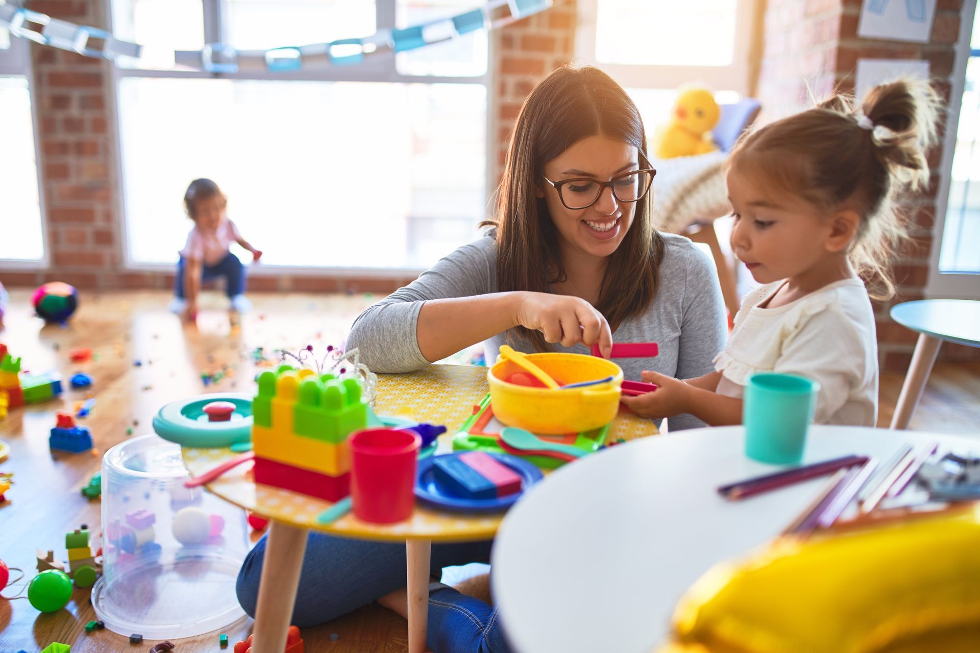 Adult and child playing with colorful toys at a table in a bright playroom