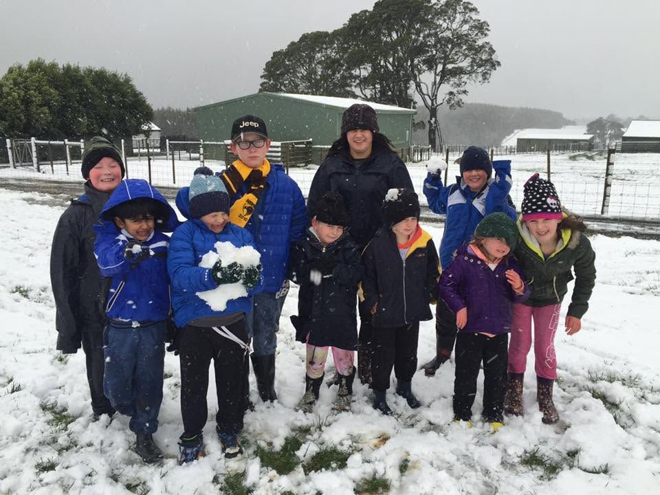 Group of children and two adults standing in snow, some holding a snowball, outdoors on a snowy day.