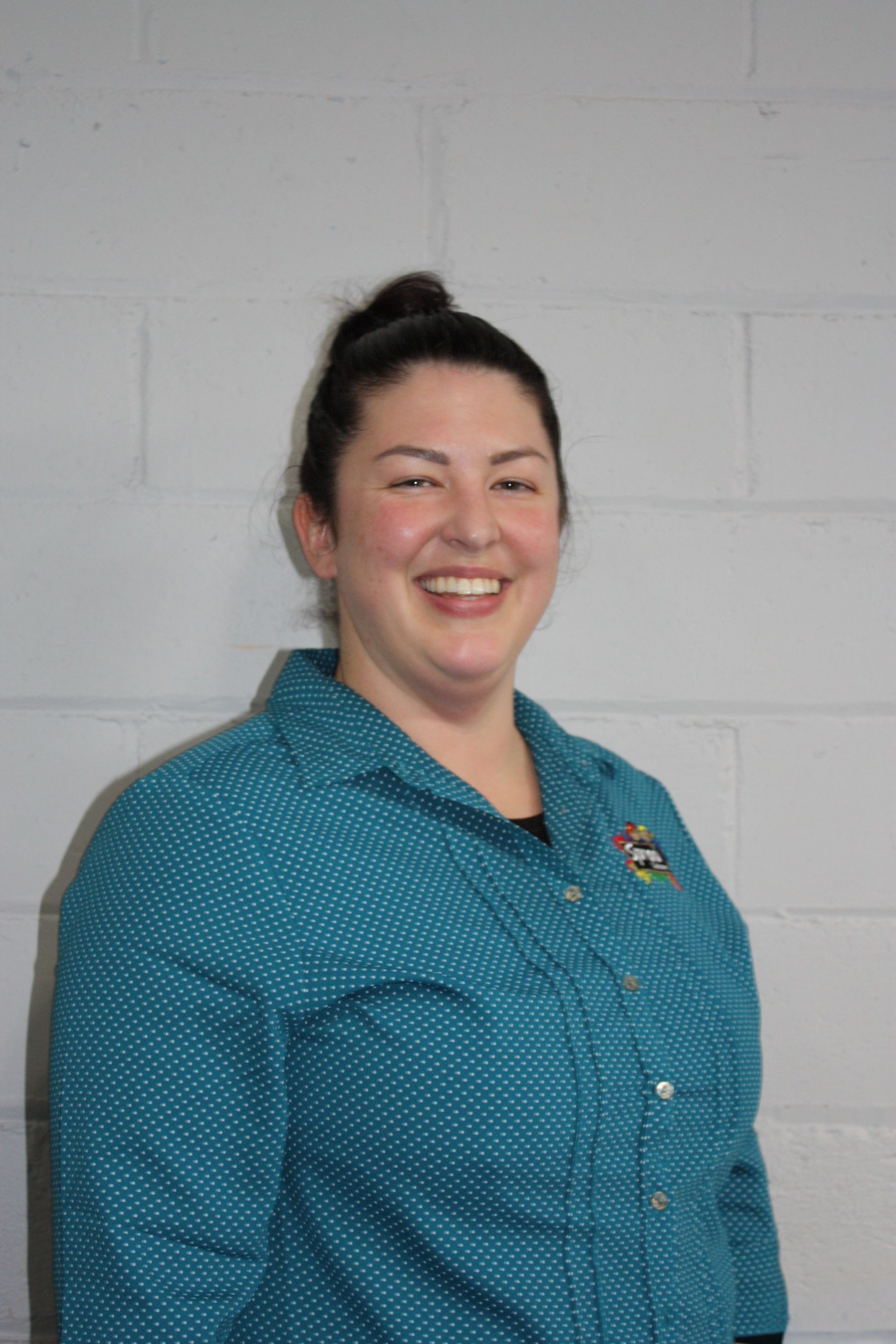Smiling person in a teal button-up shirt standing against a light gray wall