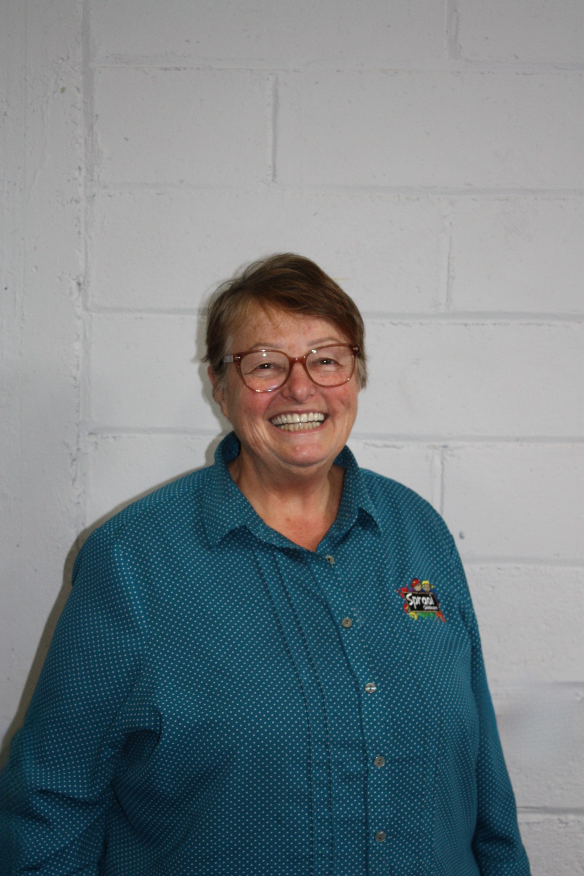 Smiling person in a teal shirt standing against a white brick wall