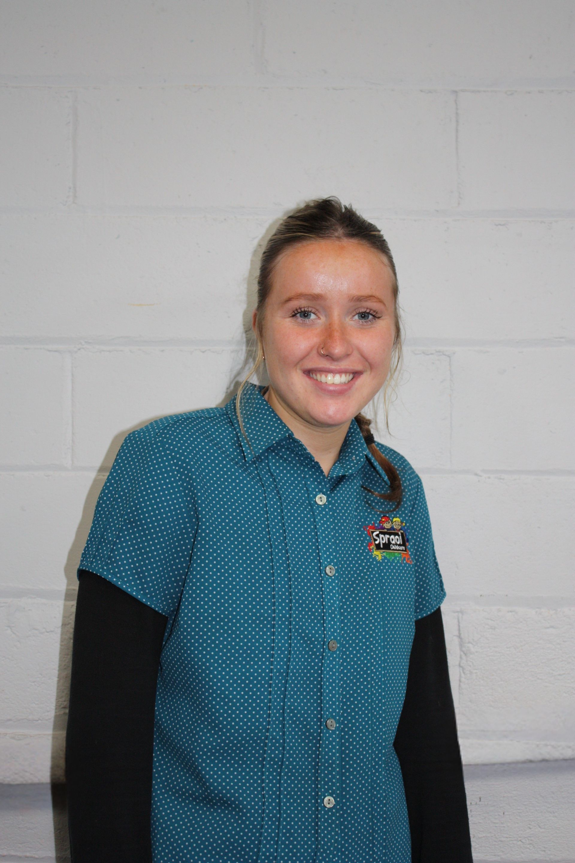 Smiling person in a teal patterned shirt standing against a light gray wall