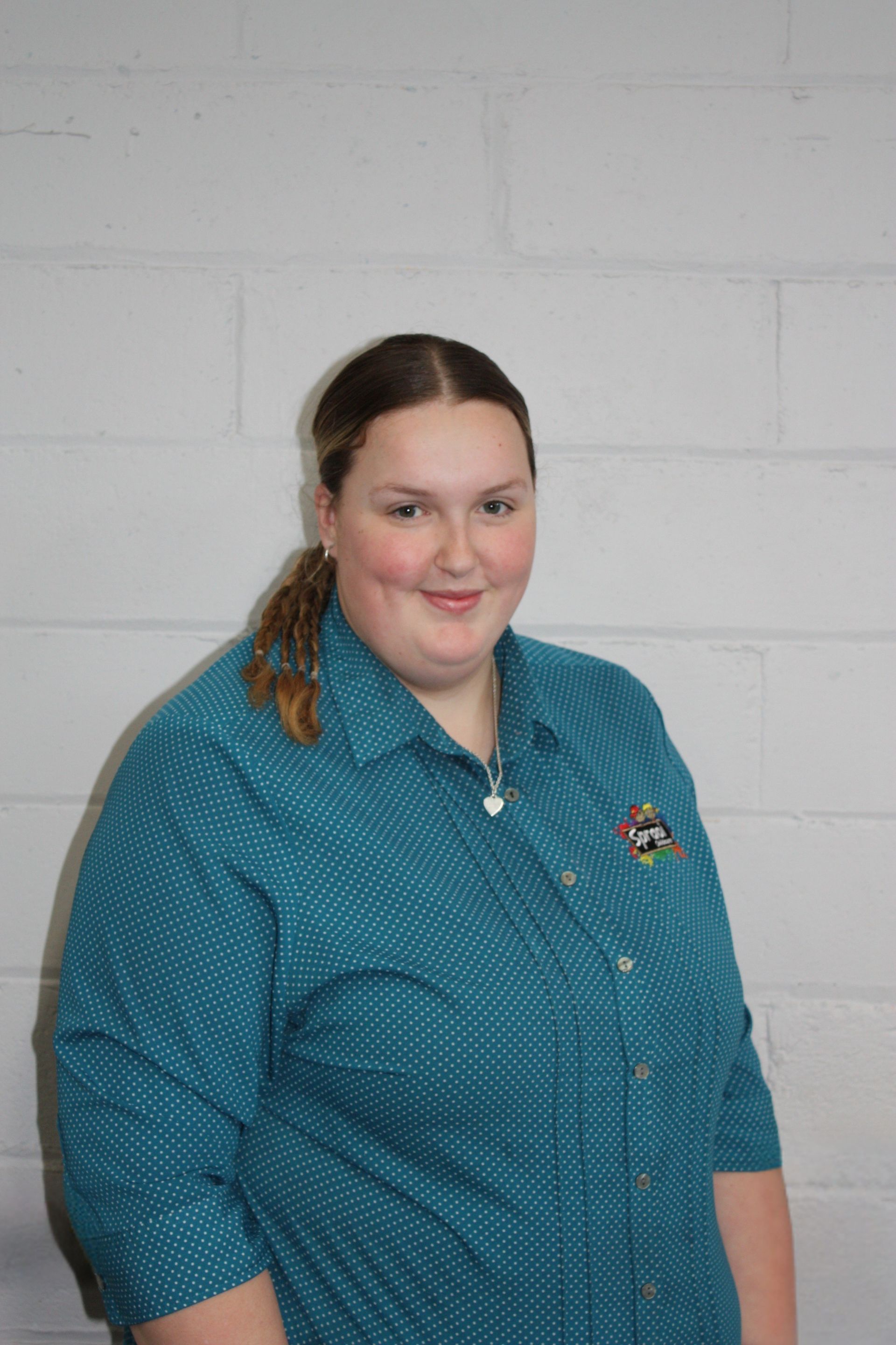 Person in a teal shirt smiling against a light gray brick wall.