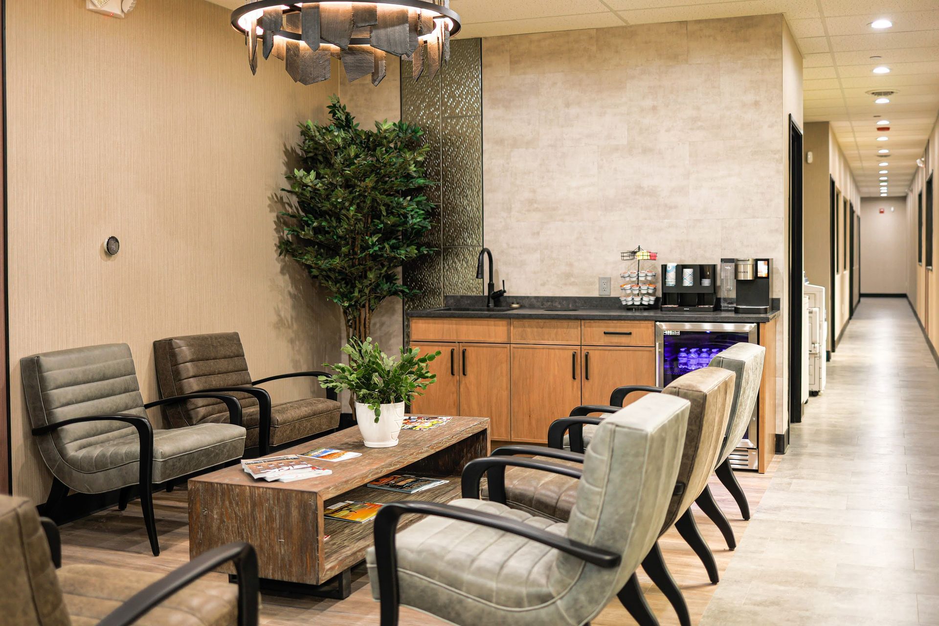 Modern waiting area with beige chairs, wooden tables, a counter, and a hallway in the background