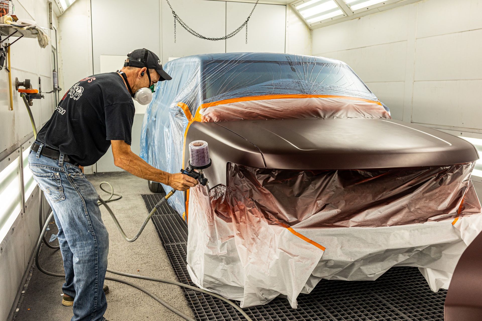 Person spray-painting a car in a workshop, masked and wearing protective gear