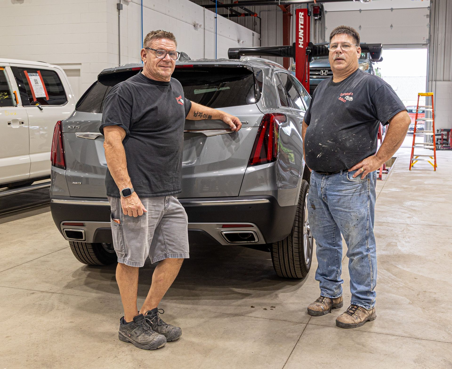 Two men standing beside a gray SUV in an auto repair shop