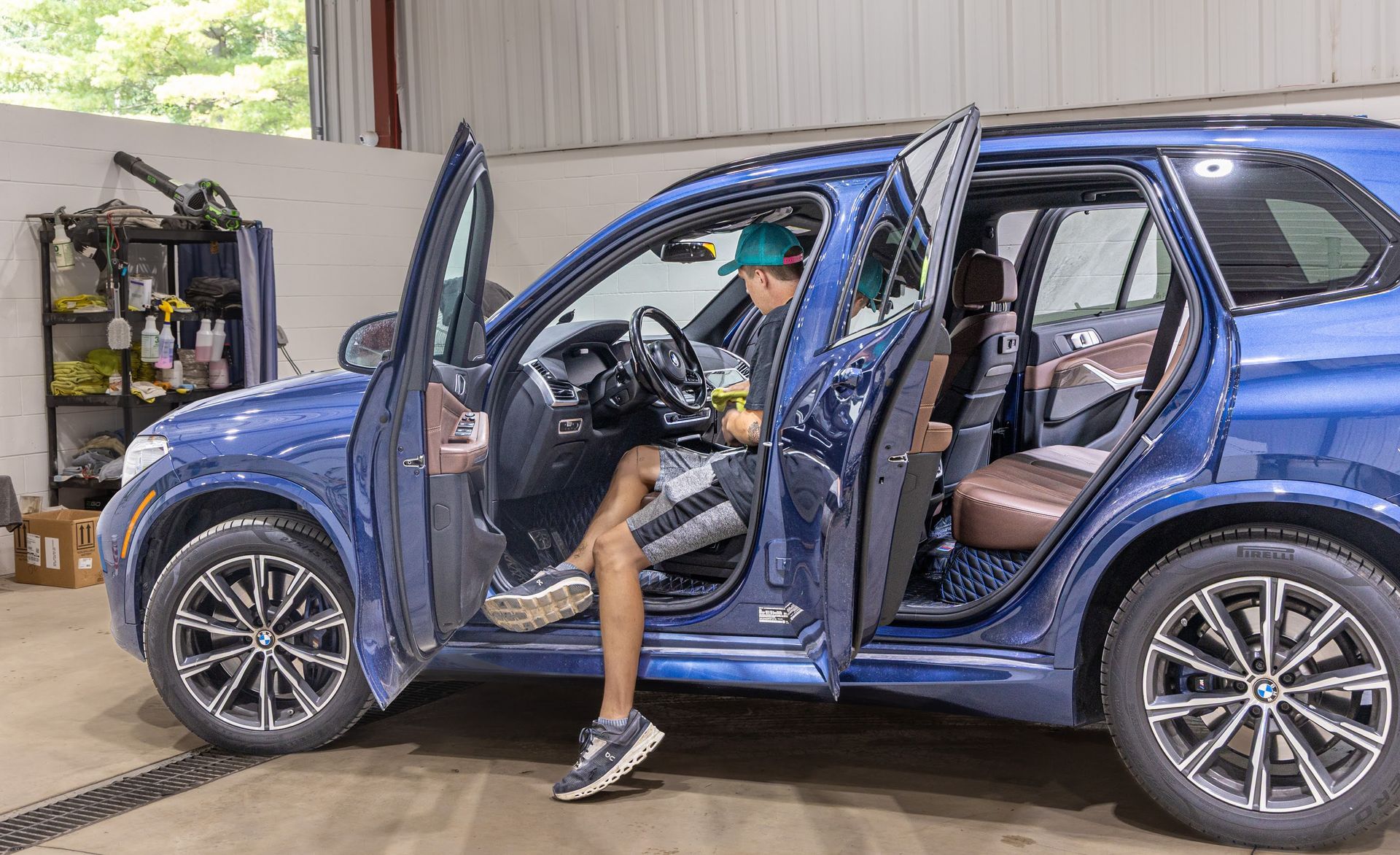 Blue SUV with both doors open; a person sits in the driver’s seat in a garage.