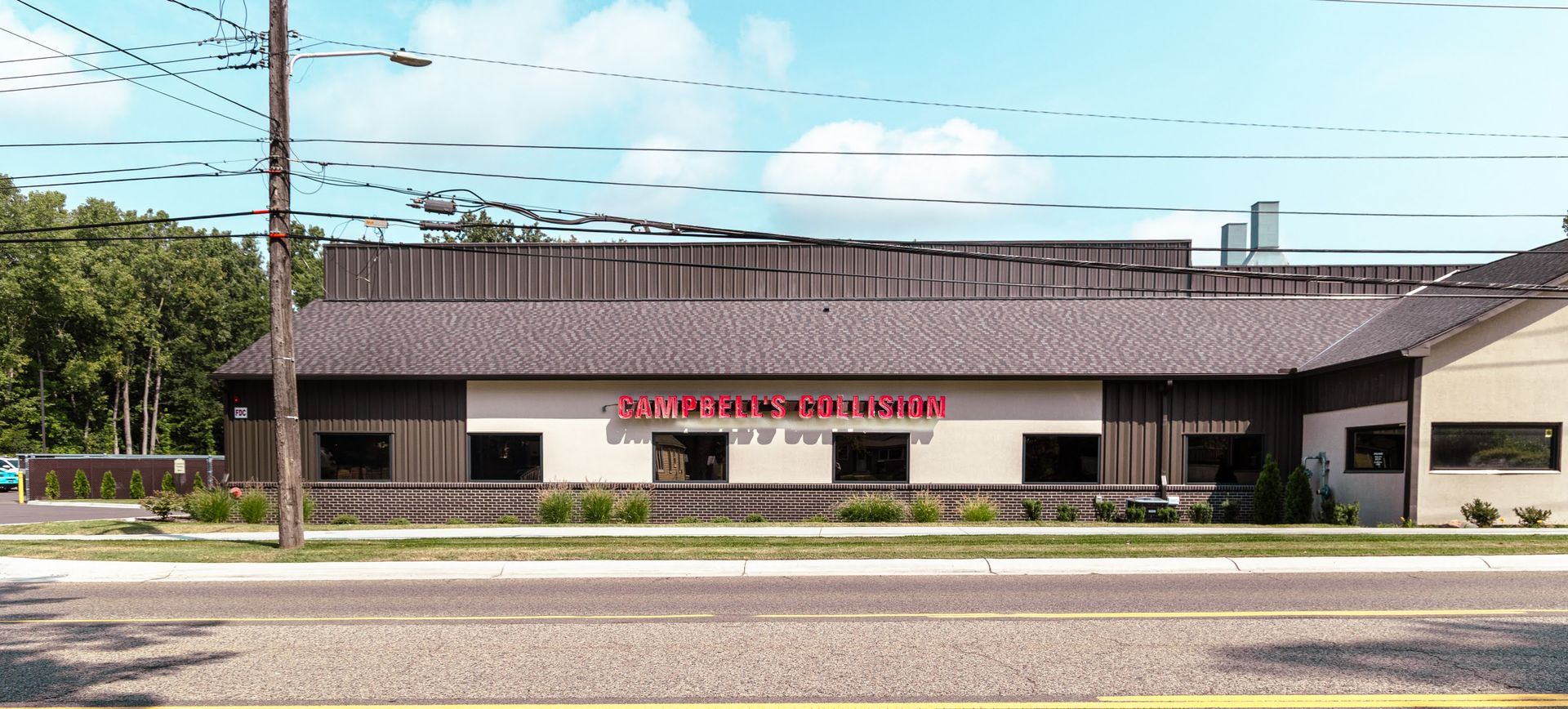 Low, single-story commercial building with a red sign, fronted by a sidewalk and street under a blue sky