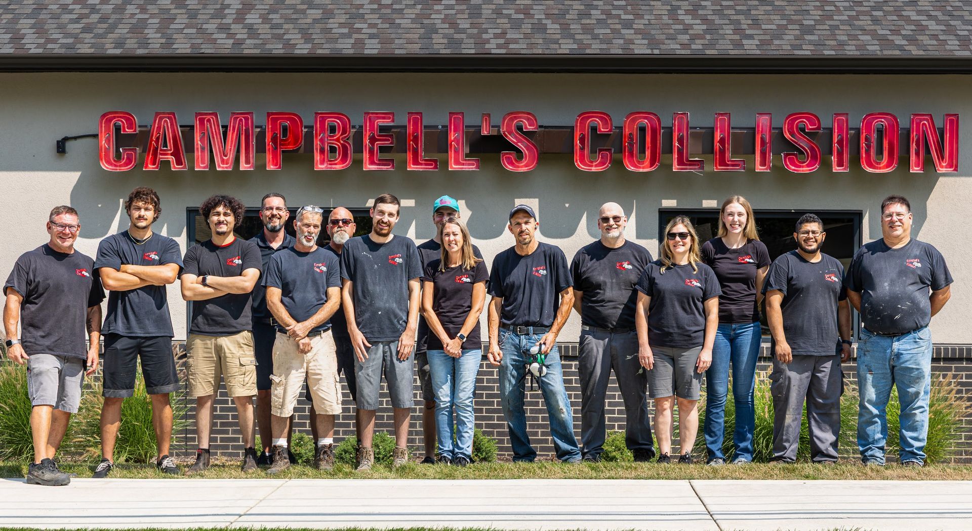 Group of employees standing outside Campbell’s Collision in front of a red sign