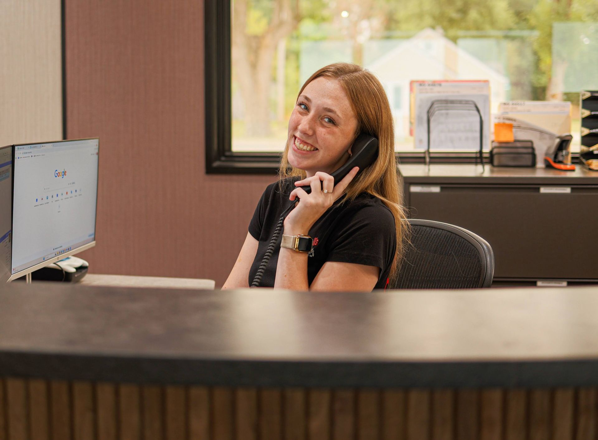 Woman smiling while talking on a phone at a reception desk in an office lobby