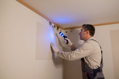 Worker using a drill to install a wall fixture near the ceiling in a room