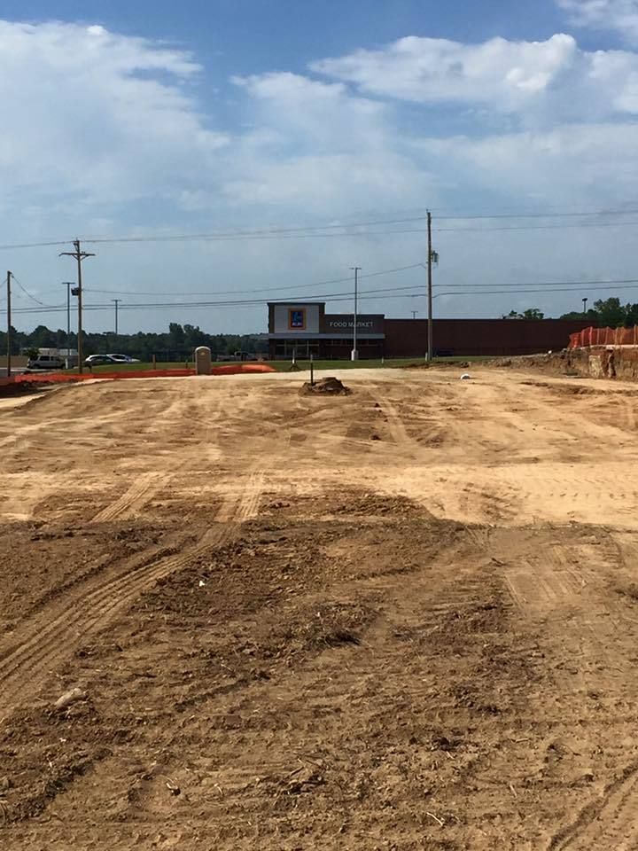 Cleared dirt lot with tire tracks, a small building in the distance, and cloudy sky overhead