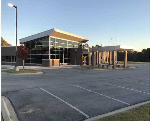 Modern building with glass facade and covered entrance beside an empty parking lot at dusk