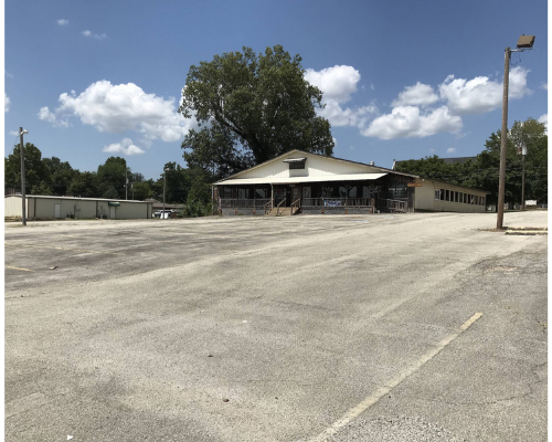 Empty gravel lot beside a low building under a bright blue sky with clouds