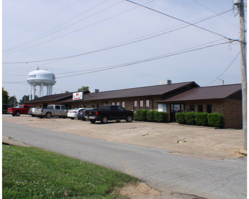 Single-story brick motel with parked cars and a water tower beside a roadside.