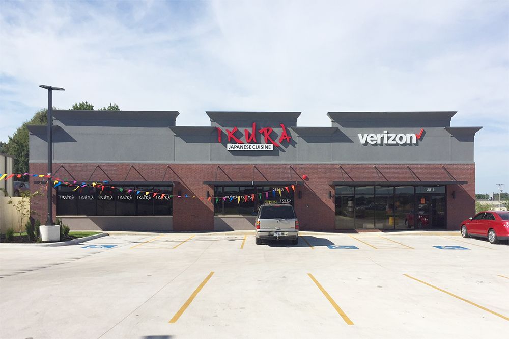 Verizon storefront in a strip mall with dark awning, parked cars, and a bright empty lot