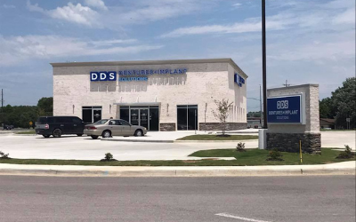 DDS office building with parked cars and a blue roadside sign under a partly cloudy sky