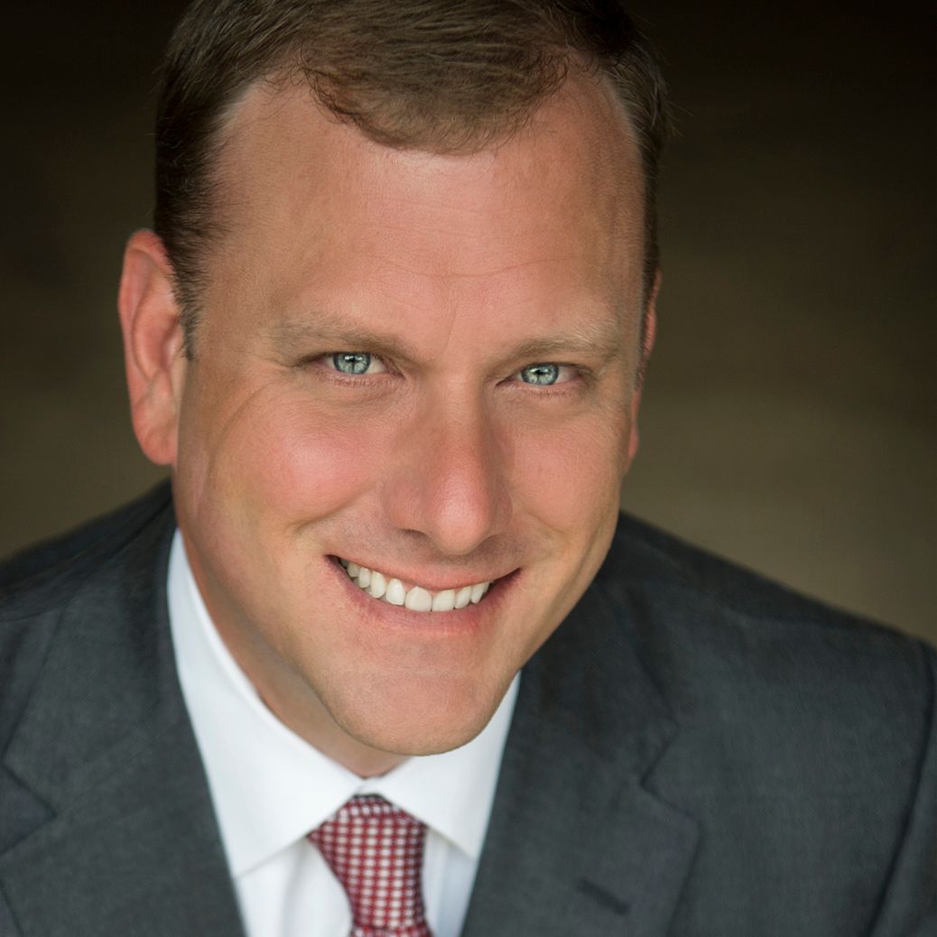 Studio headshot of a smiling man in a gray suit and red tie