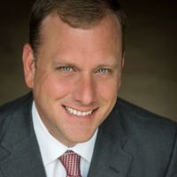 Studio headshot of a smiling man in a gray suit and red tie