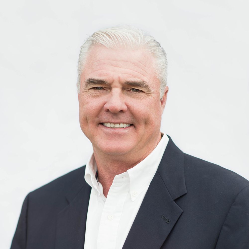 Smiling man in a navy blazer and white shirt against a light background