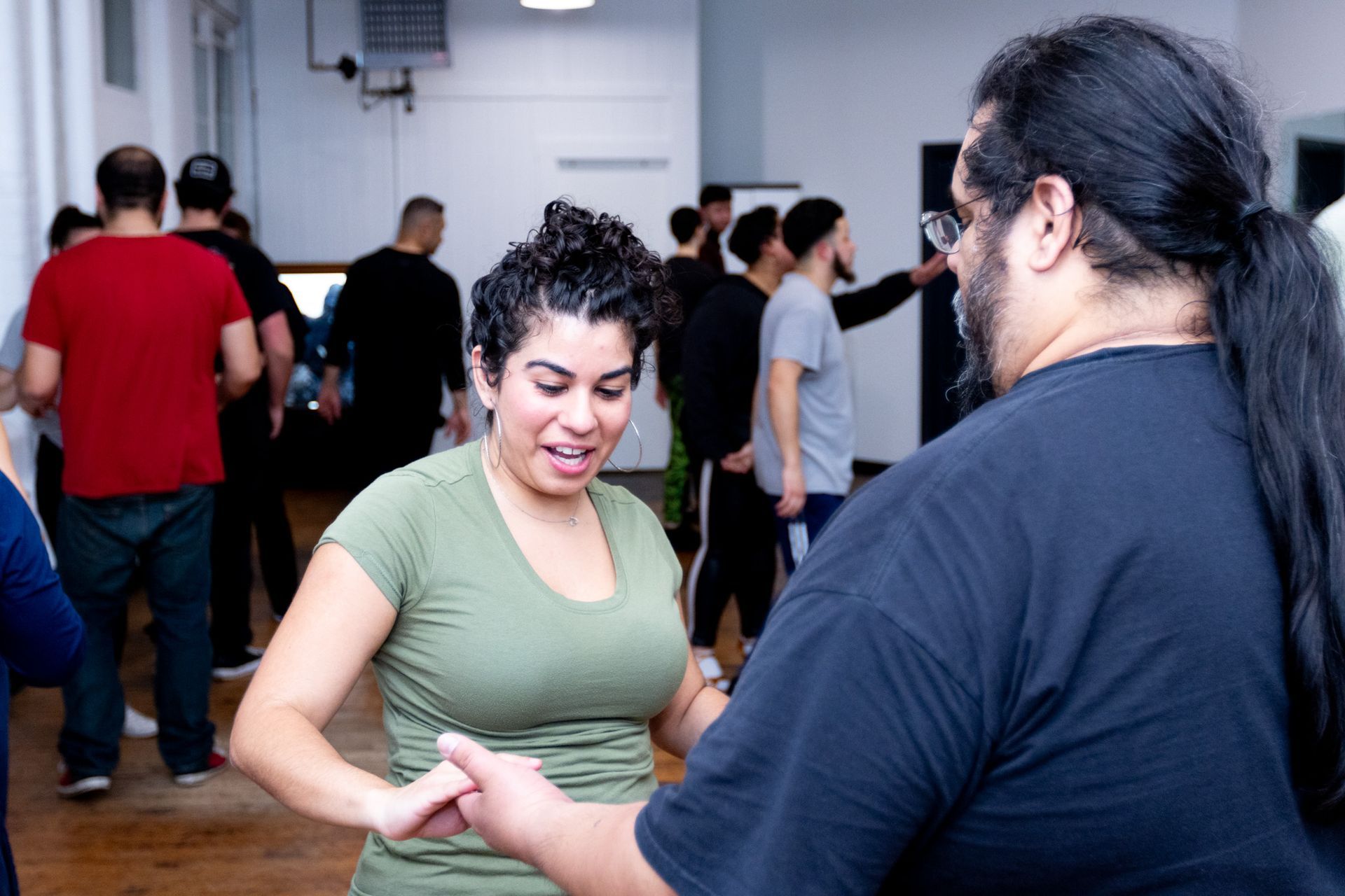 A female students smiles as she holds hands with her male dance partner during a Bachata class.