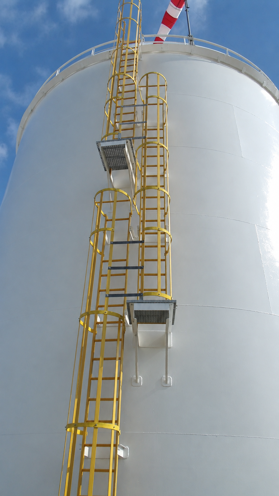 A top-down view of metal grating stairs with yellow railings leading to a work platform above water.