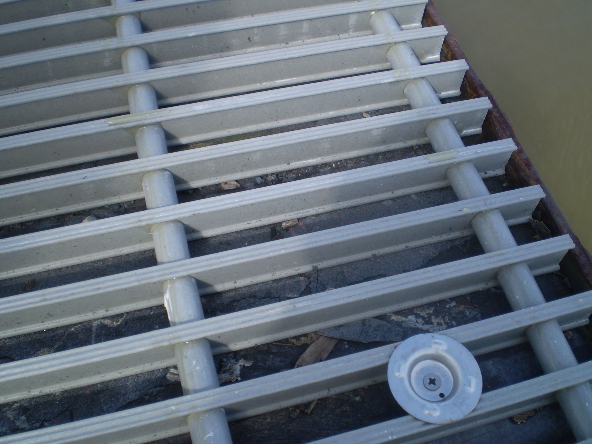 A close-up of a gray, square-grid industrial fiberglass grating panel against a white background.