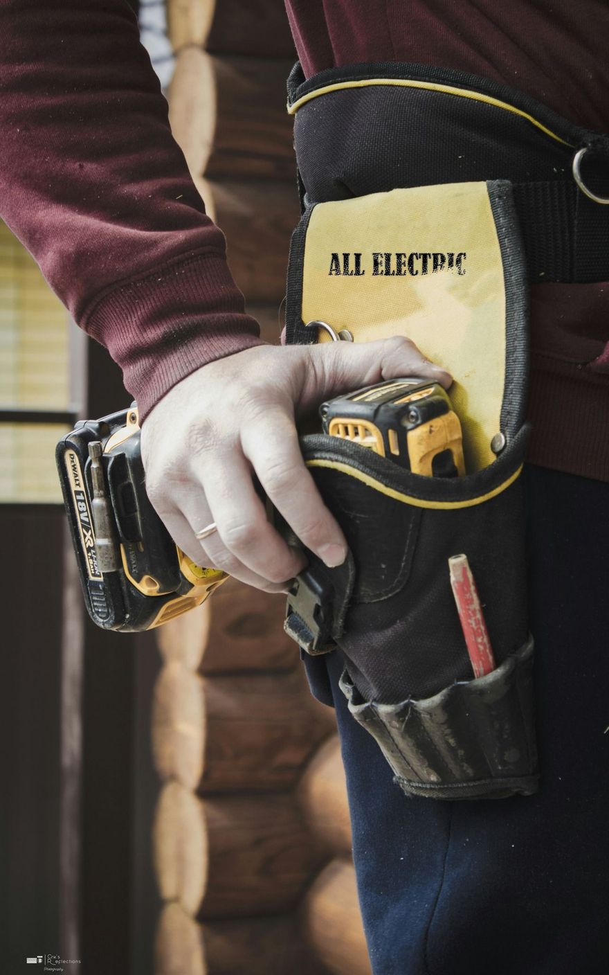 Hand in work glove holding a yellow tool on a black utility belt with pockets and tools