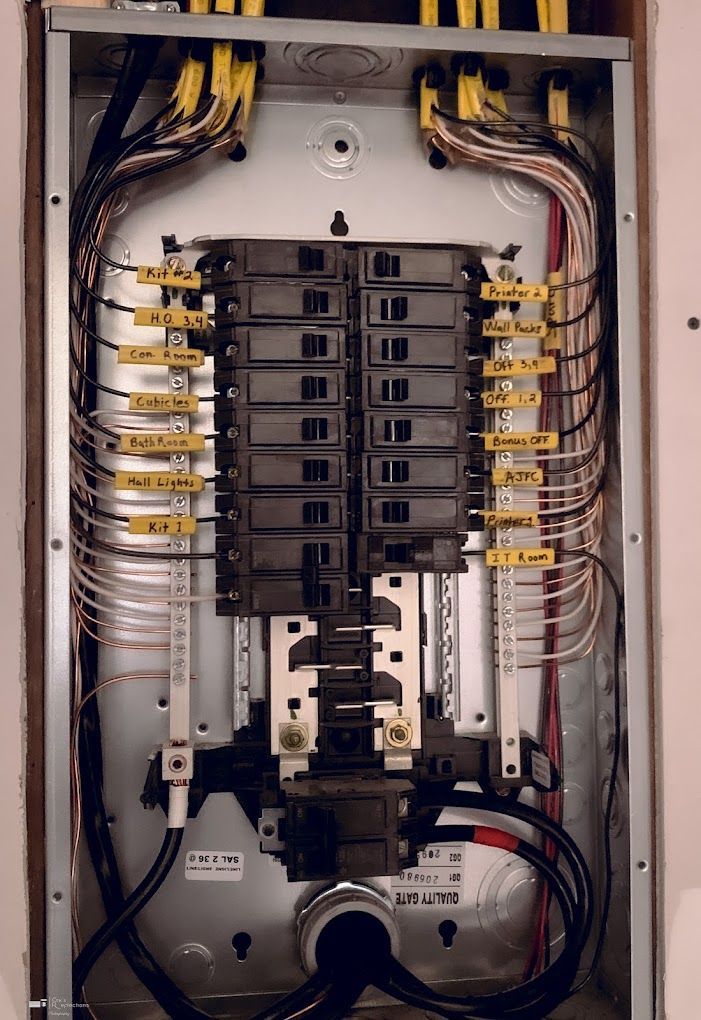 Electrical breaker panel with rows of black breakers and exposed wiring inside an open cabinet