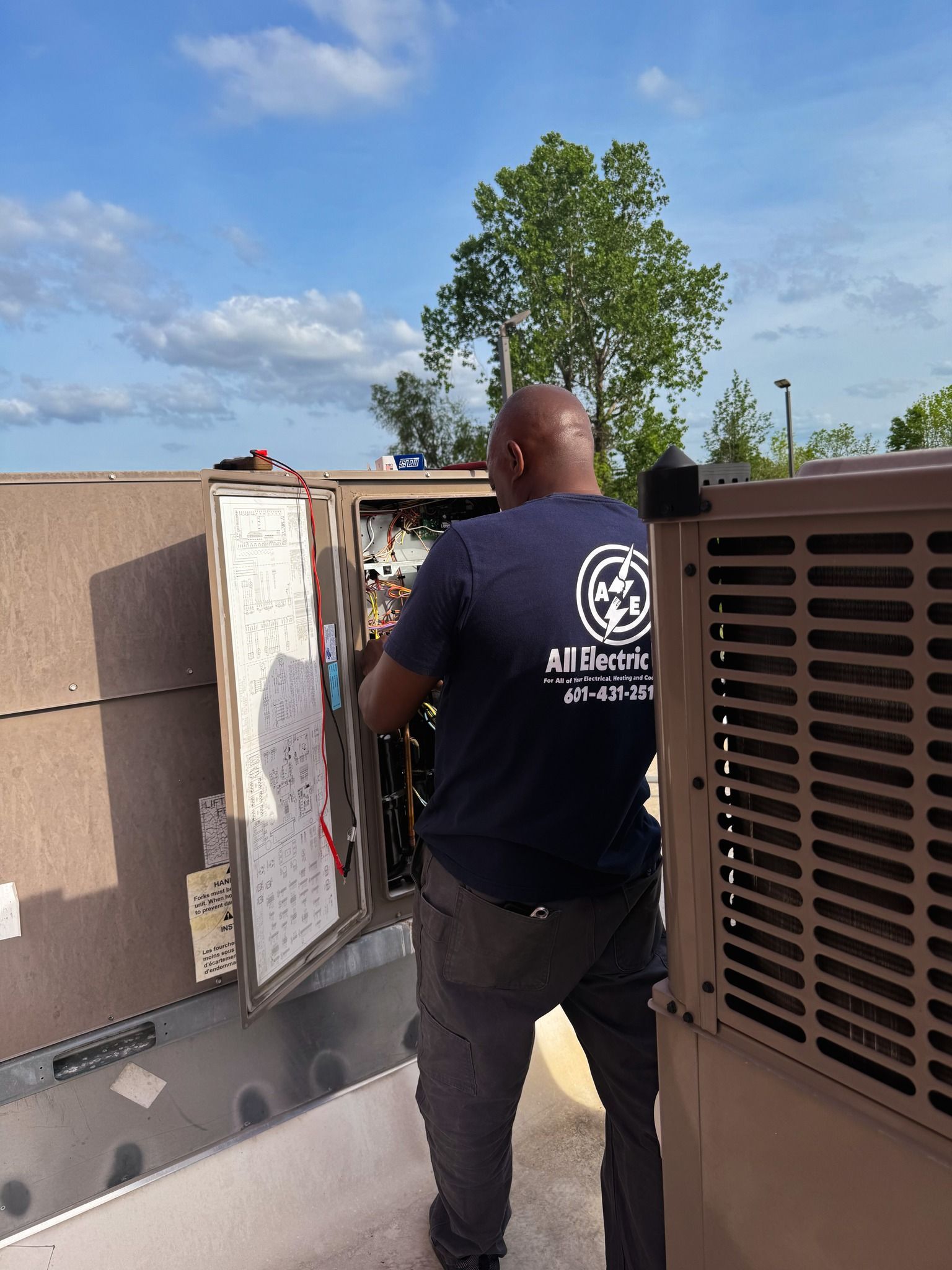 Worker inspecting rooftop HVAC unit beside an open service panel on a sunny day