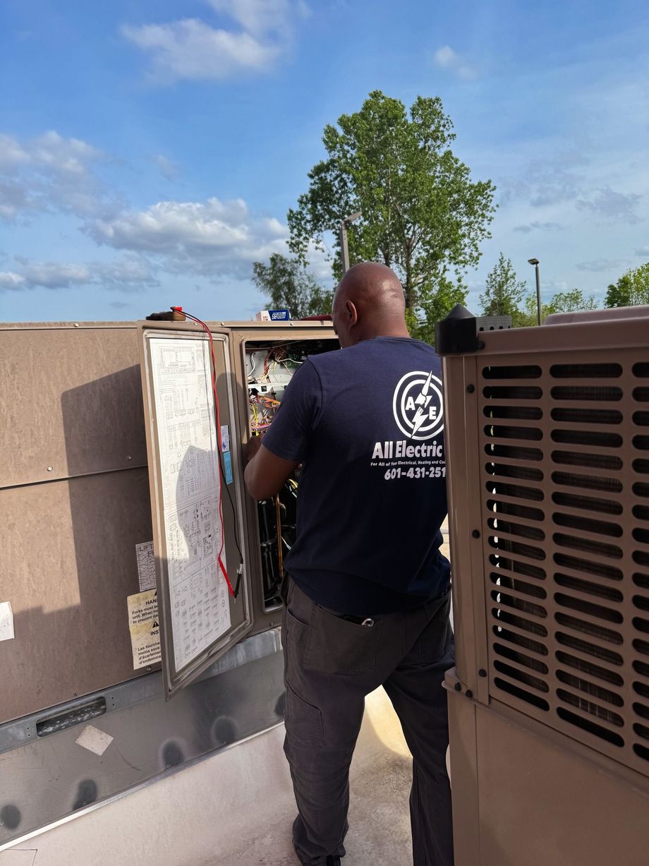 Technician inspecting rooftop HVAC unit beside a tan building under a blue sky.