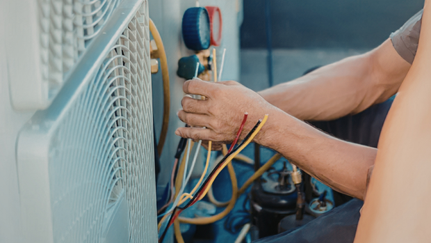 Technician repairing HVAC unit, connecting colored wires beside an outdoor air conditioner.