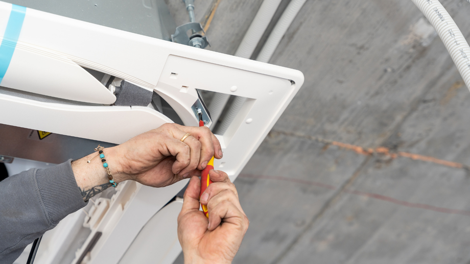 Hands using a screwdriver to install a white ceiling fixture against a concrete ceiling.