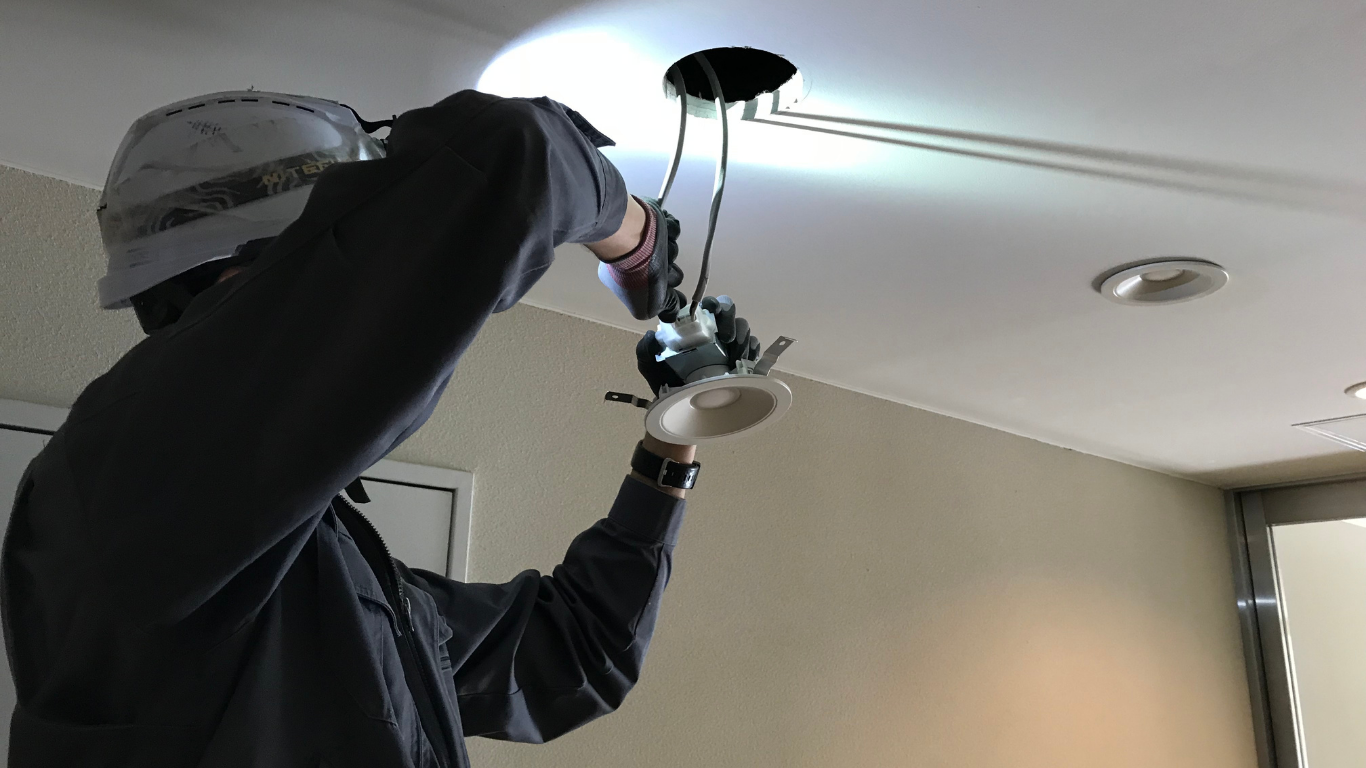Person using a drill to install a ceiling light fixture indoors