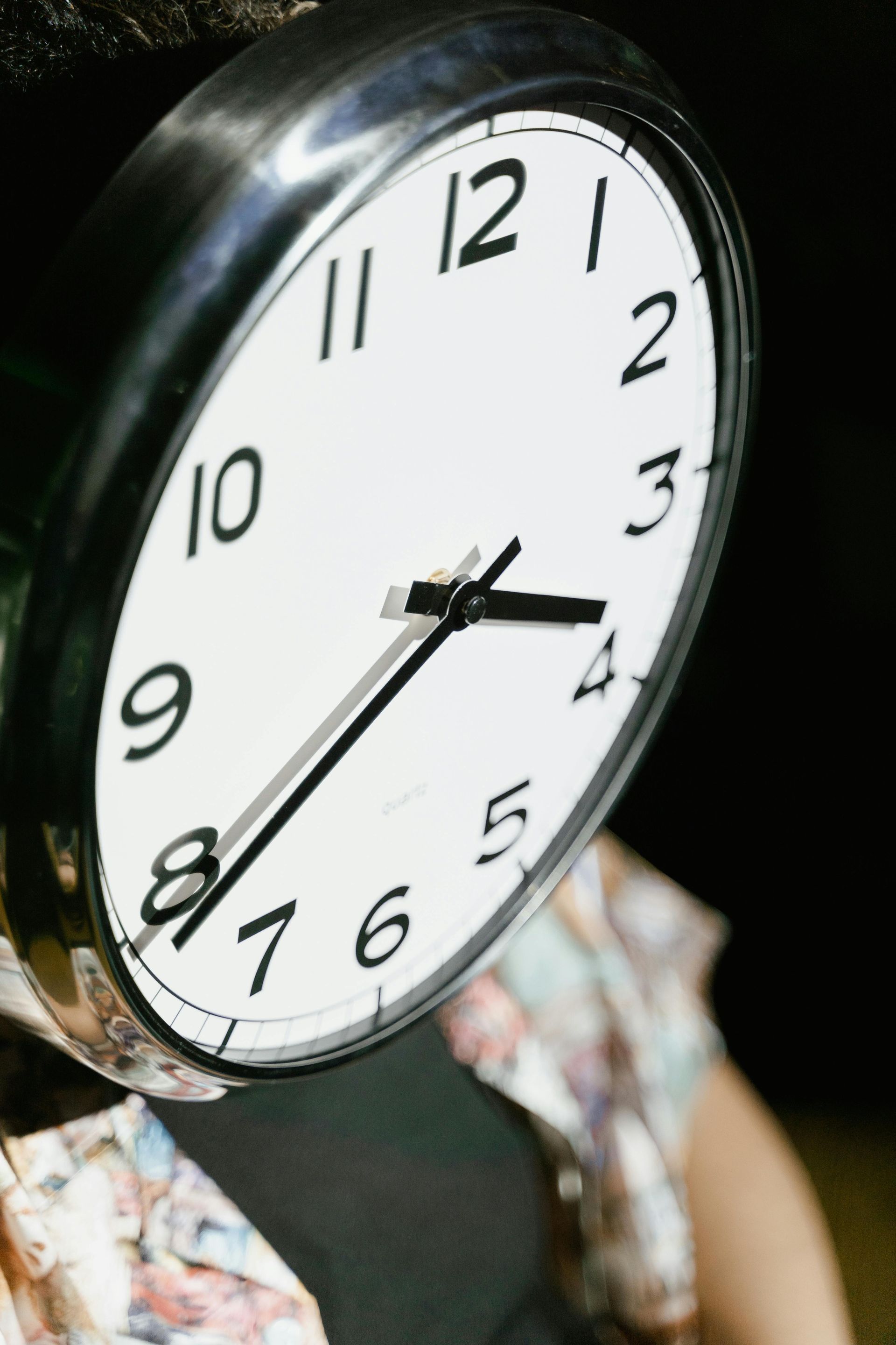 Nærbilde av en hvit analog klokke med svarte tall og visere, som viser omtrent 4:40.