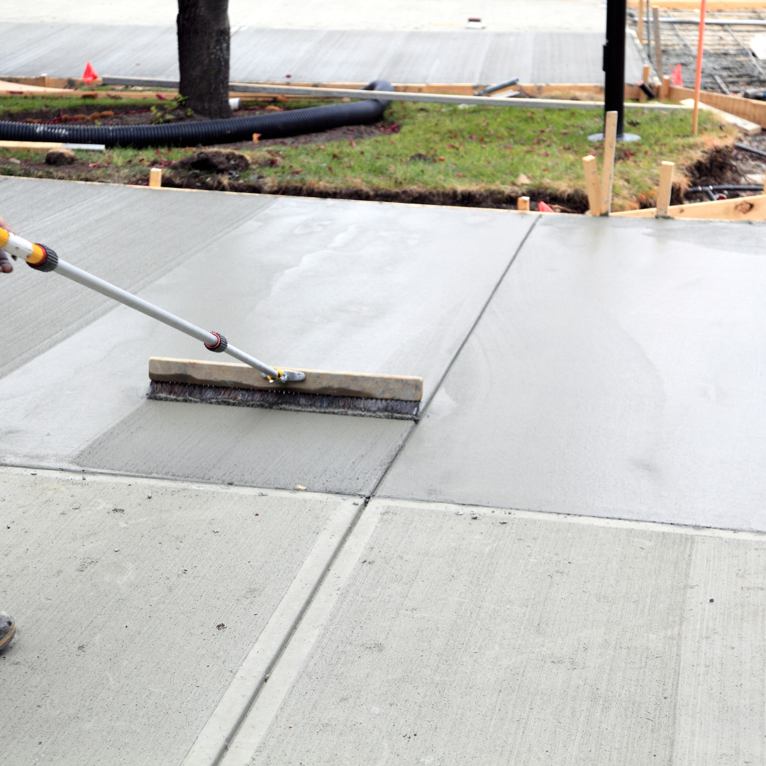 A person is using a broom to spread concrete on a sidewalk