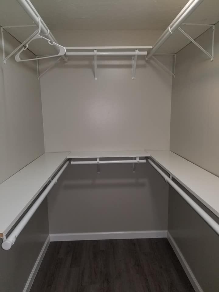 An empty walk in closet with white shelves and clothes racks.