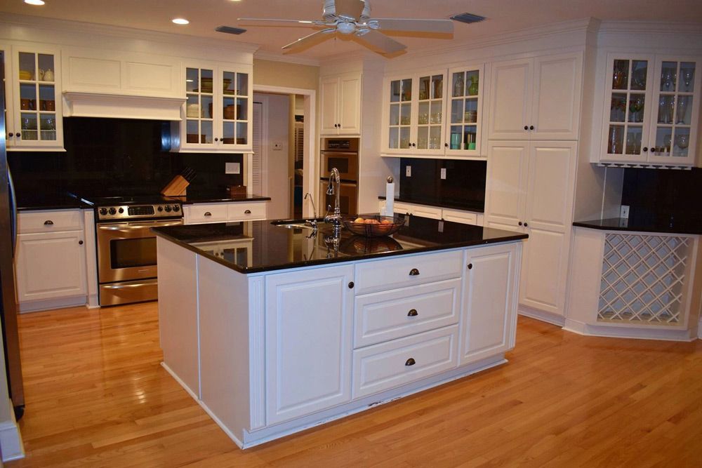 A kitchen with white cabinets and black counter tops and a large island.