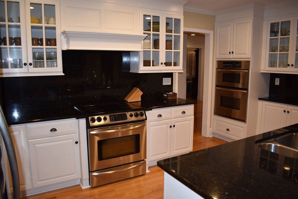 A kitchen with white cabinets , black counter tops , stainless steel appliances and a sink.