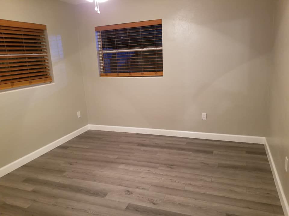 An empty room with hardwood floors and two windows.