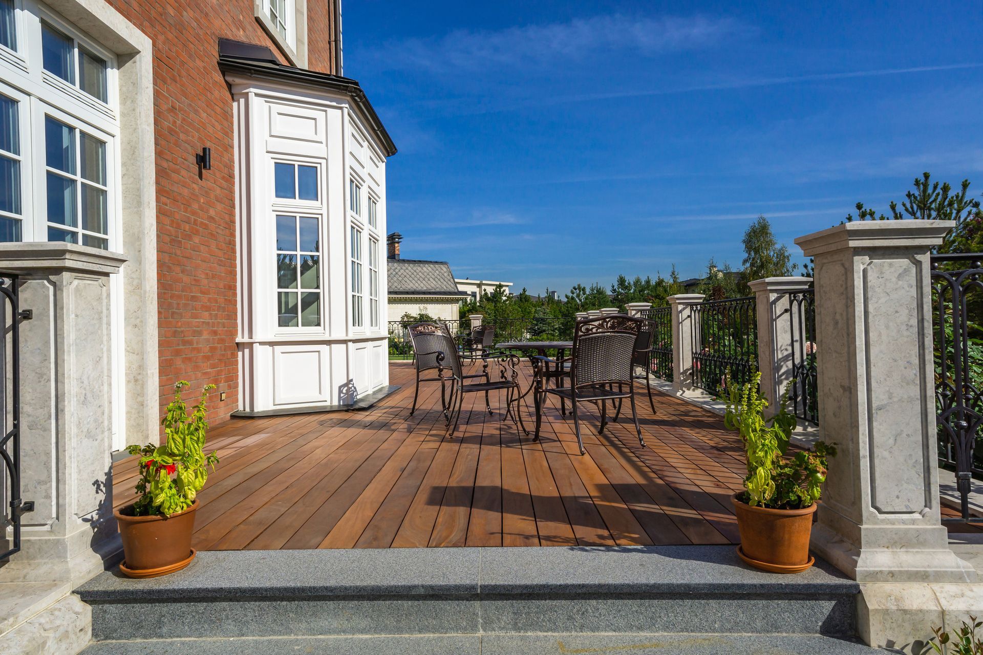 Wooden terrace with tables and chairs beside a brick house under a bright blue sky