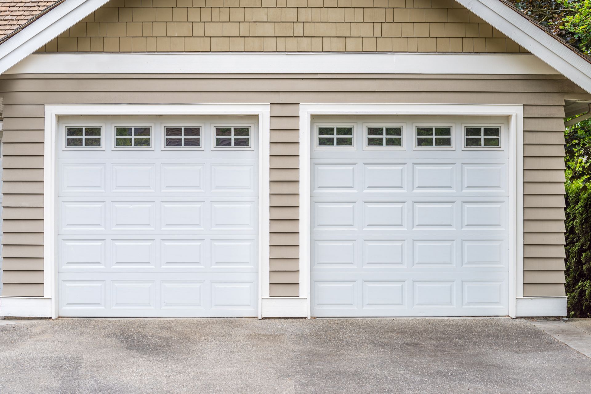Two white garage doors on a beige house exterior