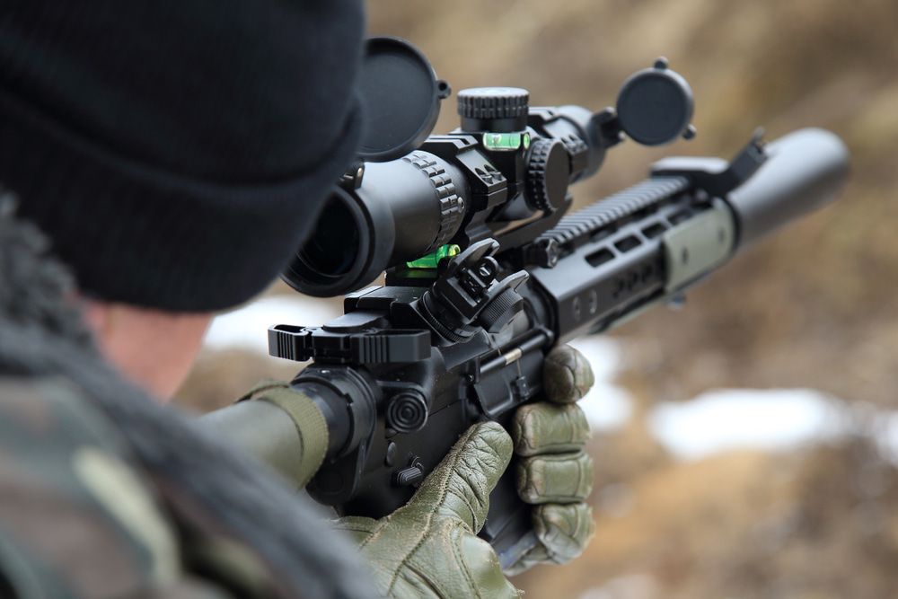 A Person Wearing Camouflage, Gloves, and a Black Hat Aims Through a Rifle Scope — Mackay Shooters Supplies in Proserpine, QLD