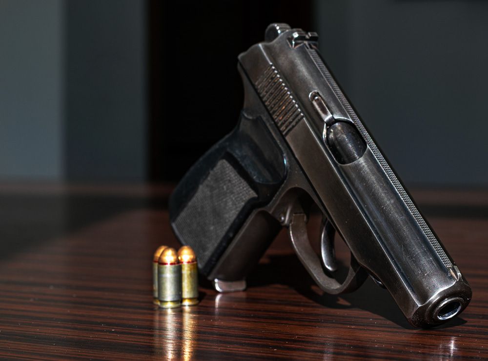 A Metallic Handgun Rests on a Wooden Surface Next to Two Bullets — Mackay Shooters Supplies in Mount Isa, QLD