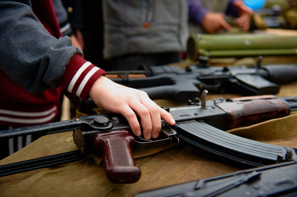 A Person Touches a Rifle on a Table Displaying Weapons — Mackay Shooters Supplies in Mount Isa, QLD