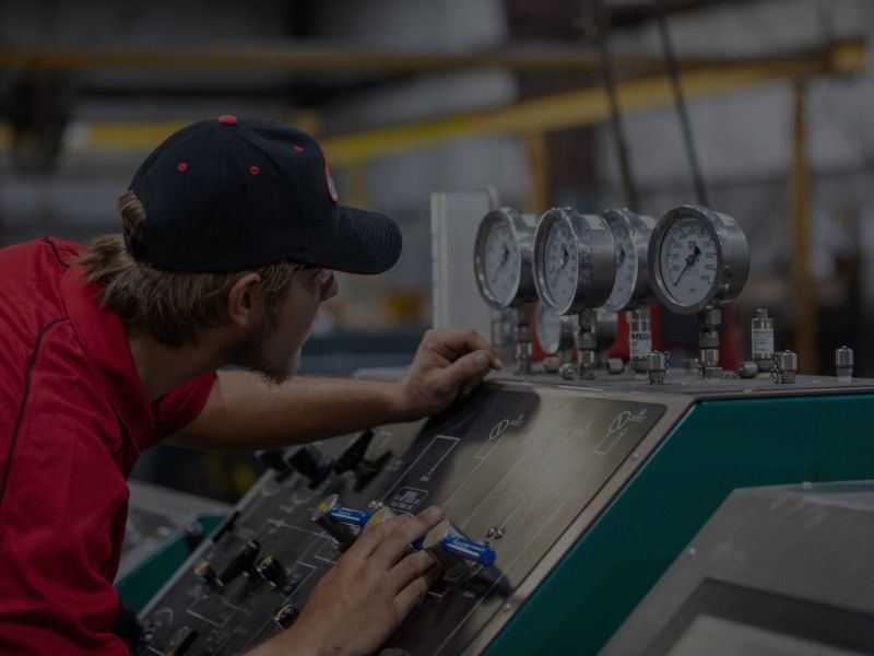 Worker in a red shirt operating industrial machinery with gauges in a workshop