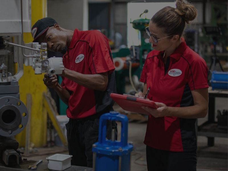 Two workers in red uniforms inspecting equipment in a factory workshop