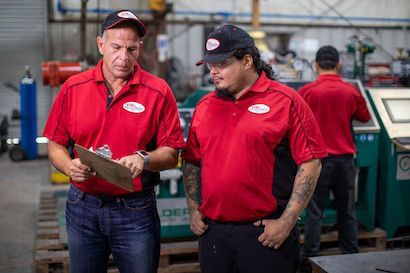 Two workers in red shirts discussing a clipboard in a factory workshop.