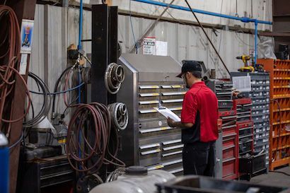 Worker in red shirt organizing papers beside tool cabinets in a workshop